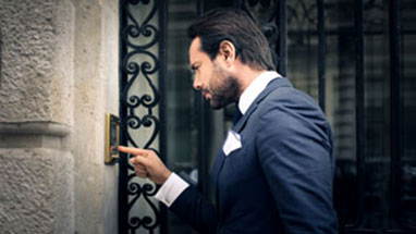 Man in a suit ringing a doorbell to advise the owner that he is about to repossess his car.